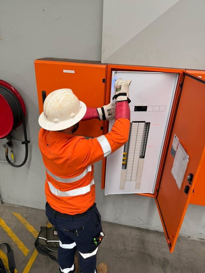 Electrician in a hard hat inspecting an industrial switchboard