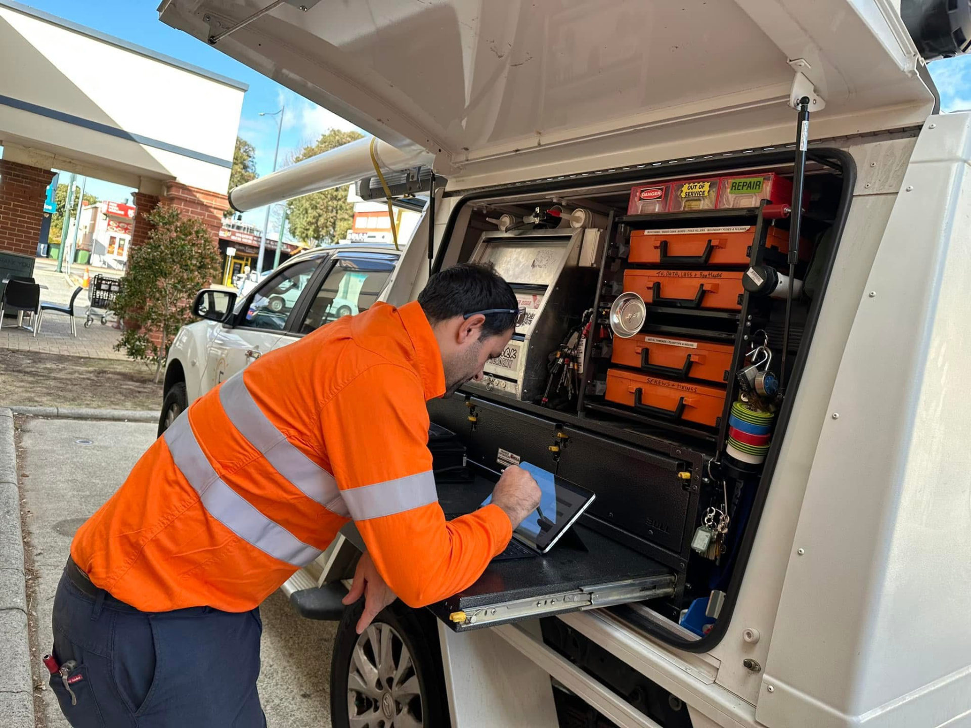 Electrician writing up a job report on a tablet at the service van